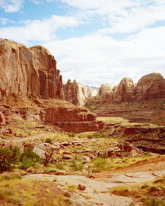 A vast desert landscape features towering red rock formations under a partly cloudy sky.