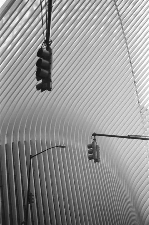Two traffic lights and a street light are visible against a modern building with a ribbed facade.