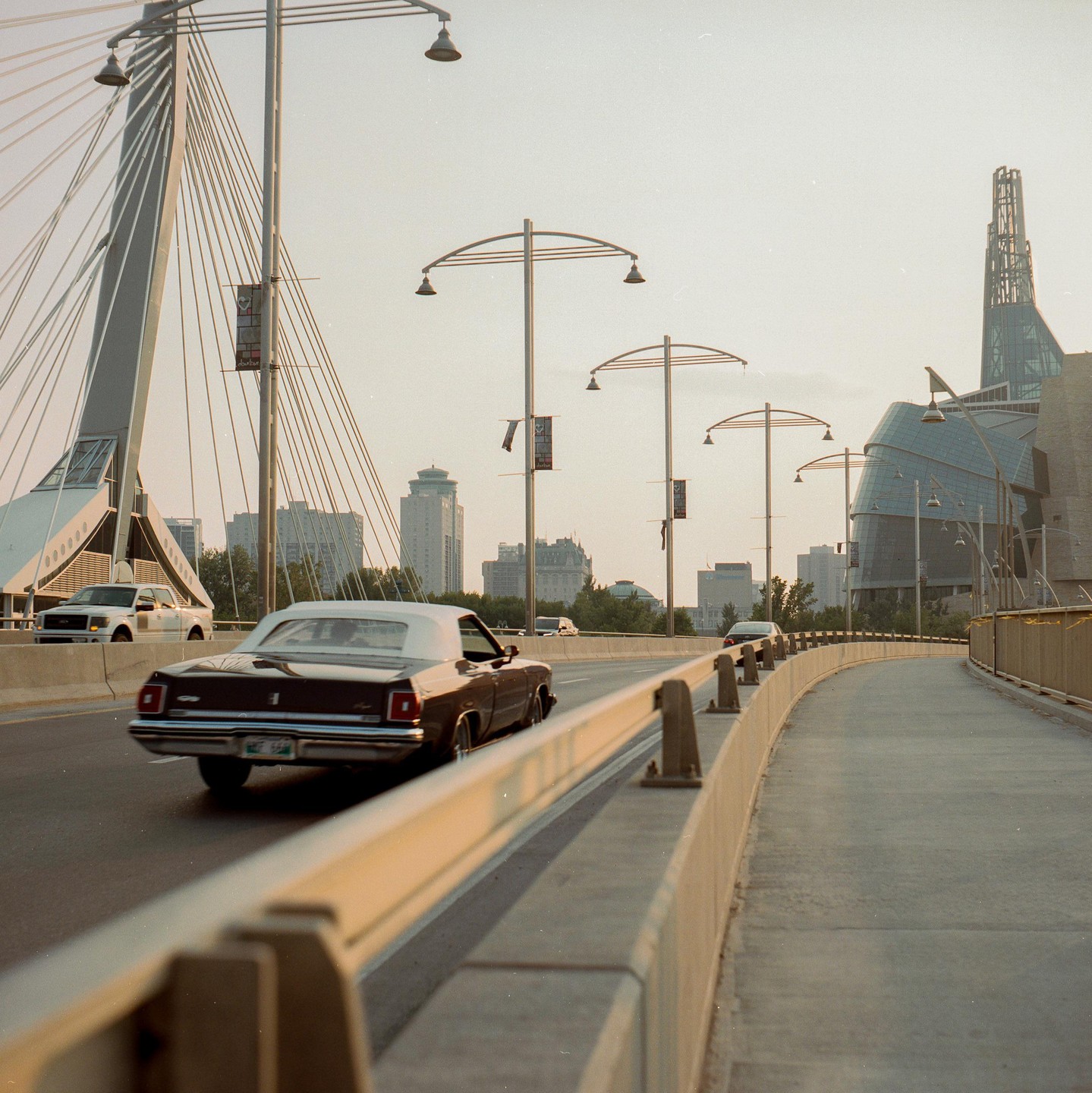 A brown convertible drives on a bridge with a modern building in the background.