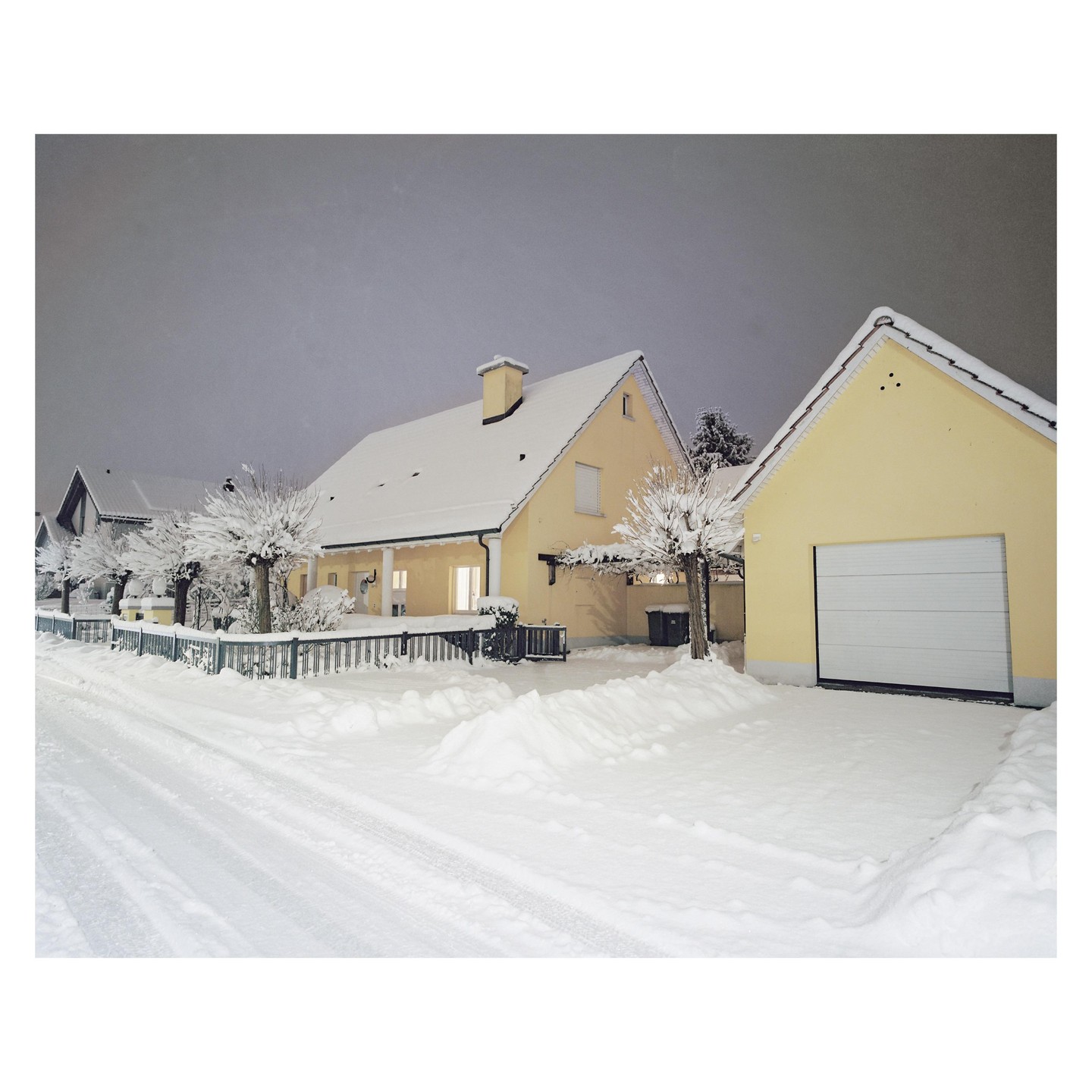 A yellow house and garage are covered in snow at night.