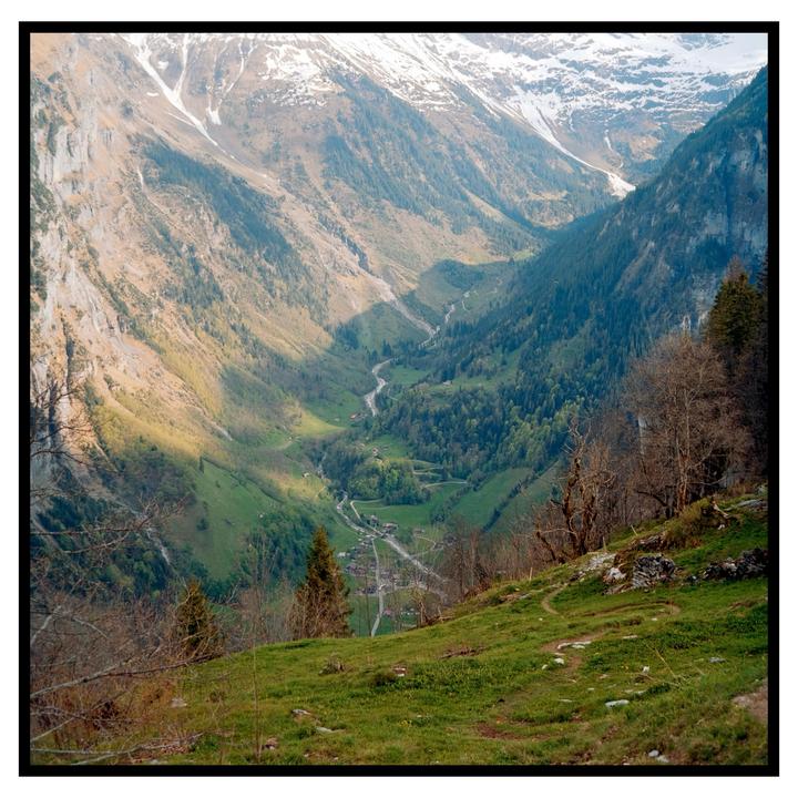 A winding river flows through a valley with a small village nestled among green trees and snow-capped mountains.