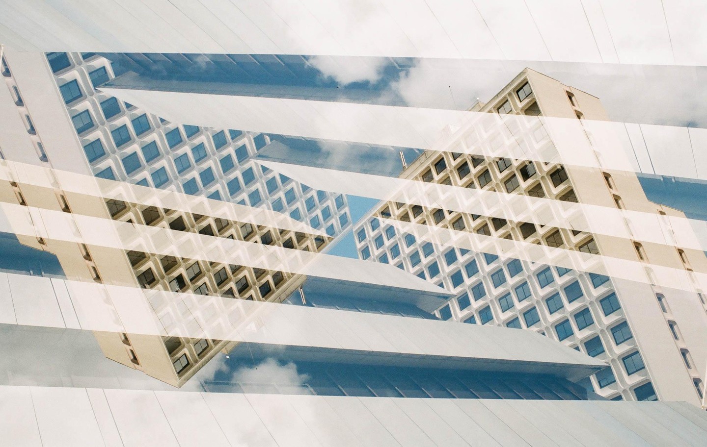 A double exposure shows two buildings with many windows and a cloudy sky.