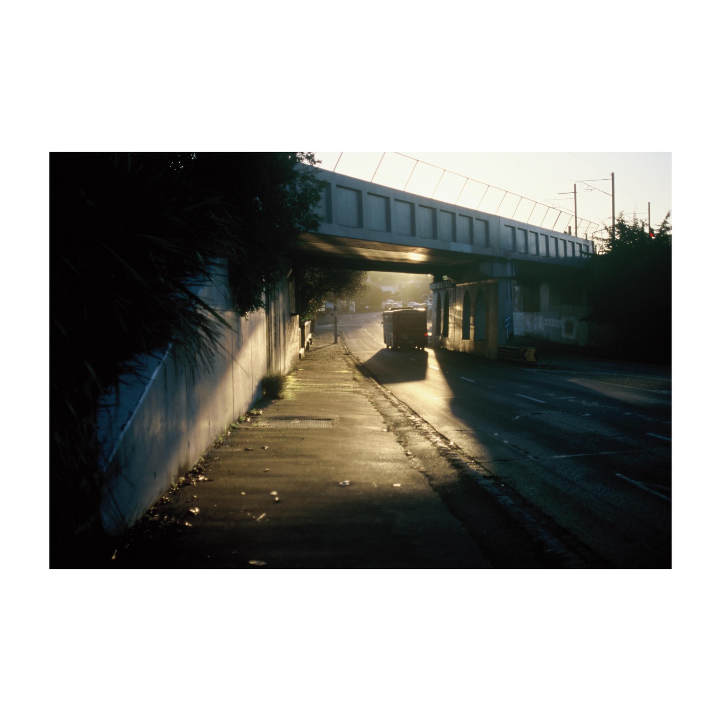 A truck drives under a concrete overpass on a street with a sidewalk on the left.