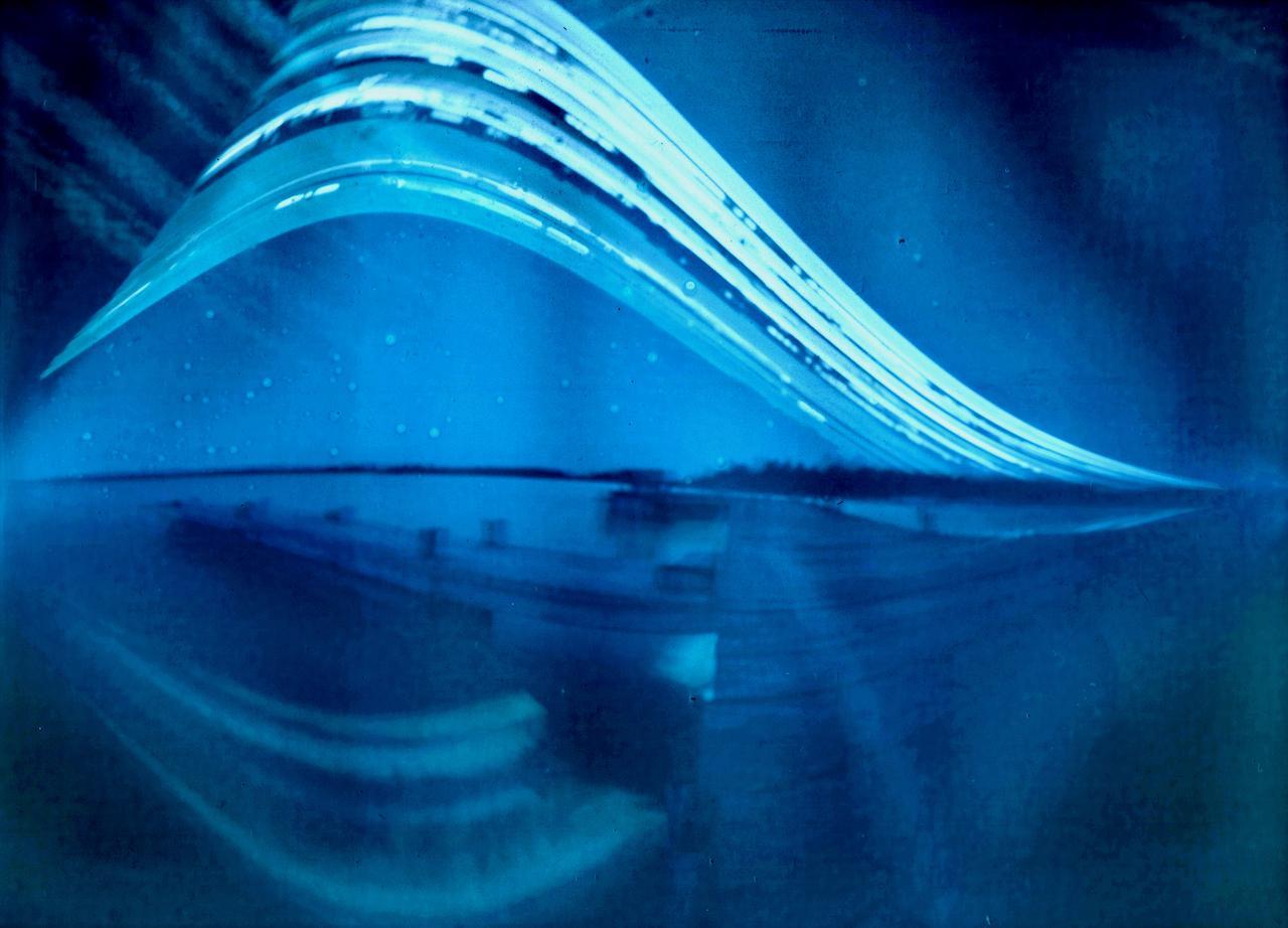 A blue-toned abstract image shows a curved light trail above a blurred landscape with reflections.