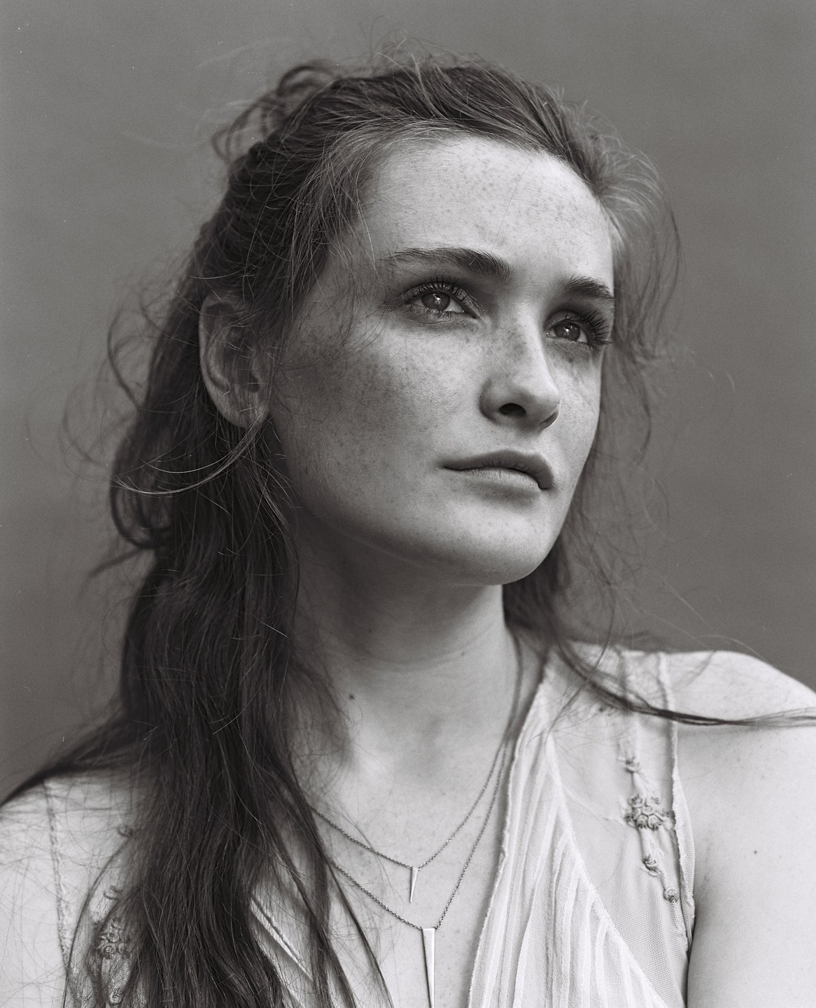 A woman with long hair and freckles looks up and to the right.