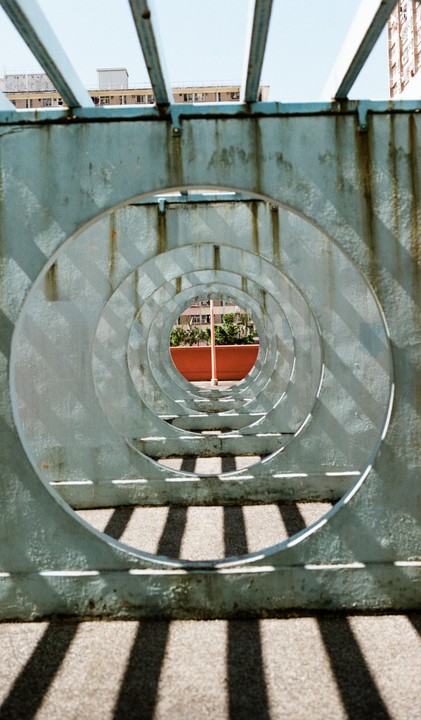 A series of concentric circles on a metal structure frames a view of buildings and trees in the distance.