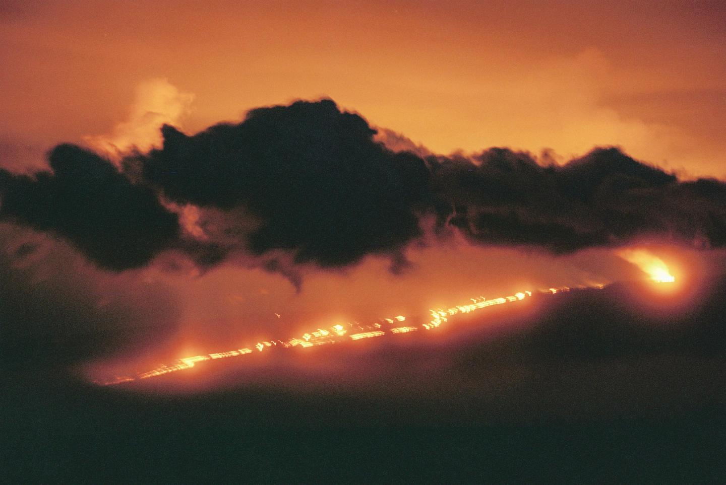 A long exposure photograph shows a glowing line of light across a dark, cloudy sky at night.