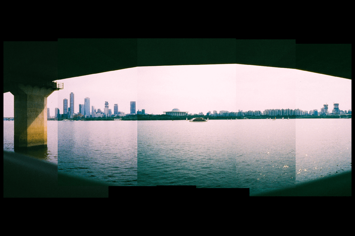 A panoramic view of a city skyline across a body of water, seen from under a bridge.
