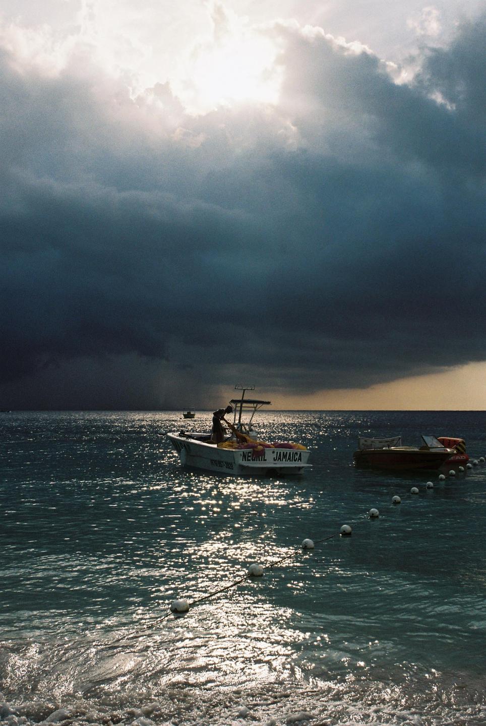 A boat with "Negril Jamaica" written on its stern is on the water under a dramatic, cloudy sky.
