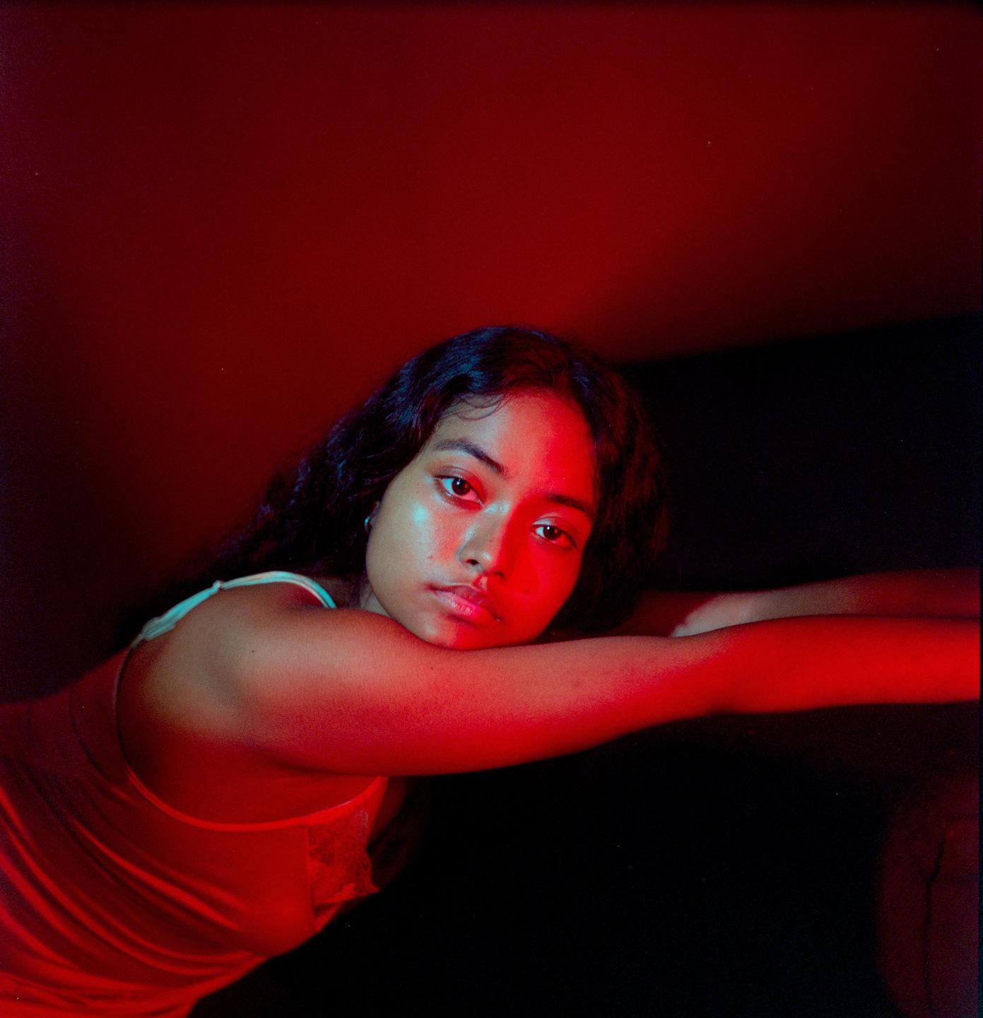A woman with dark hair rests her head on her arm, illuminated by red light.