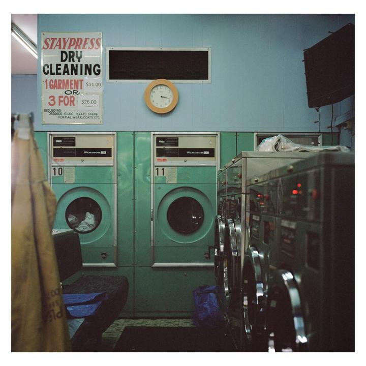 A laundromat interior features a sign for dry cleaning services above a row of washing machines.