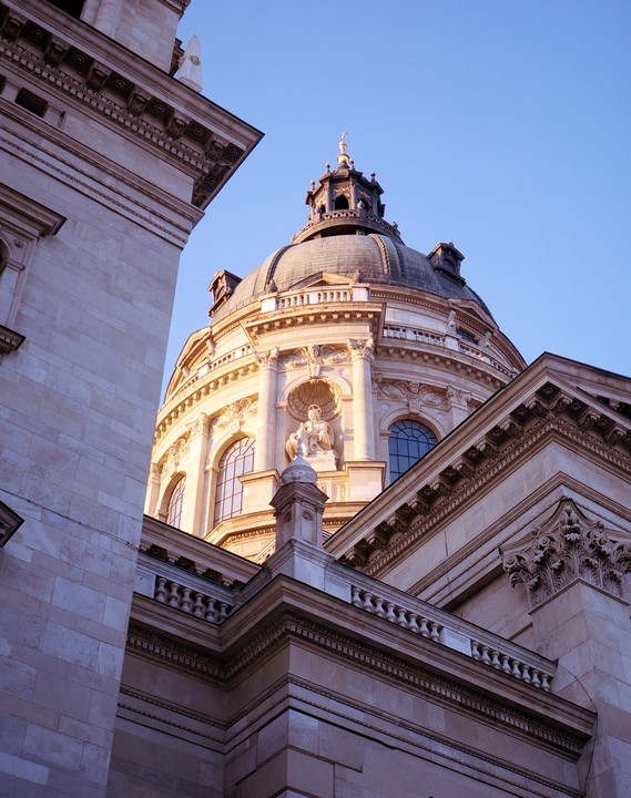 A low-angle view shows the dome and facade of a large stone building against a clear sky.