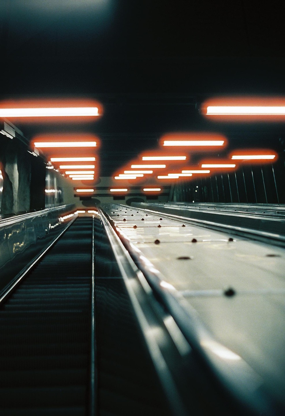An escalator leads up towards a ceiling with many bright orange lights.