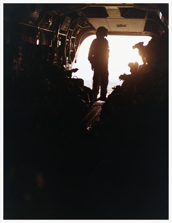 A person stands silhouetted in the open doorway of an aircraft, looking out at a bright sky.
