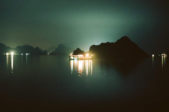 A boat with bright lights is on the water at night, surrounded by dark mountains.