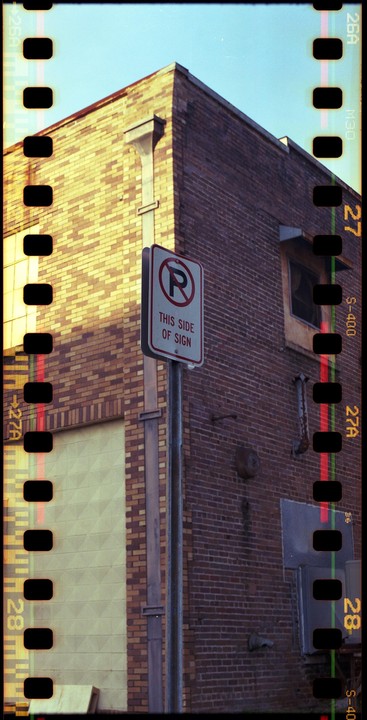 A no parking sign stands in front of a brick building with a clear blue sky overhead.