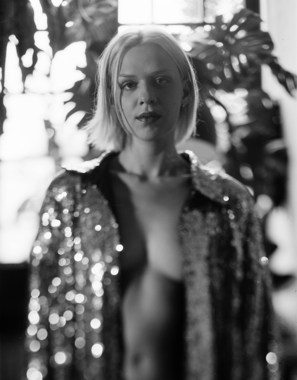 A woman with short hair wears an open sequined jacket, revealing her bare chest.