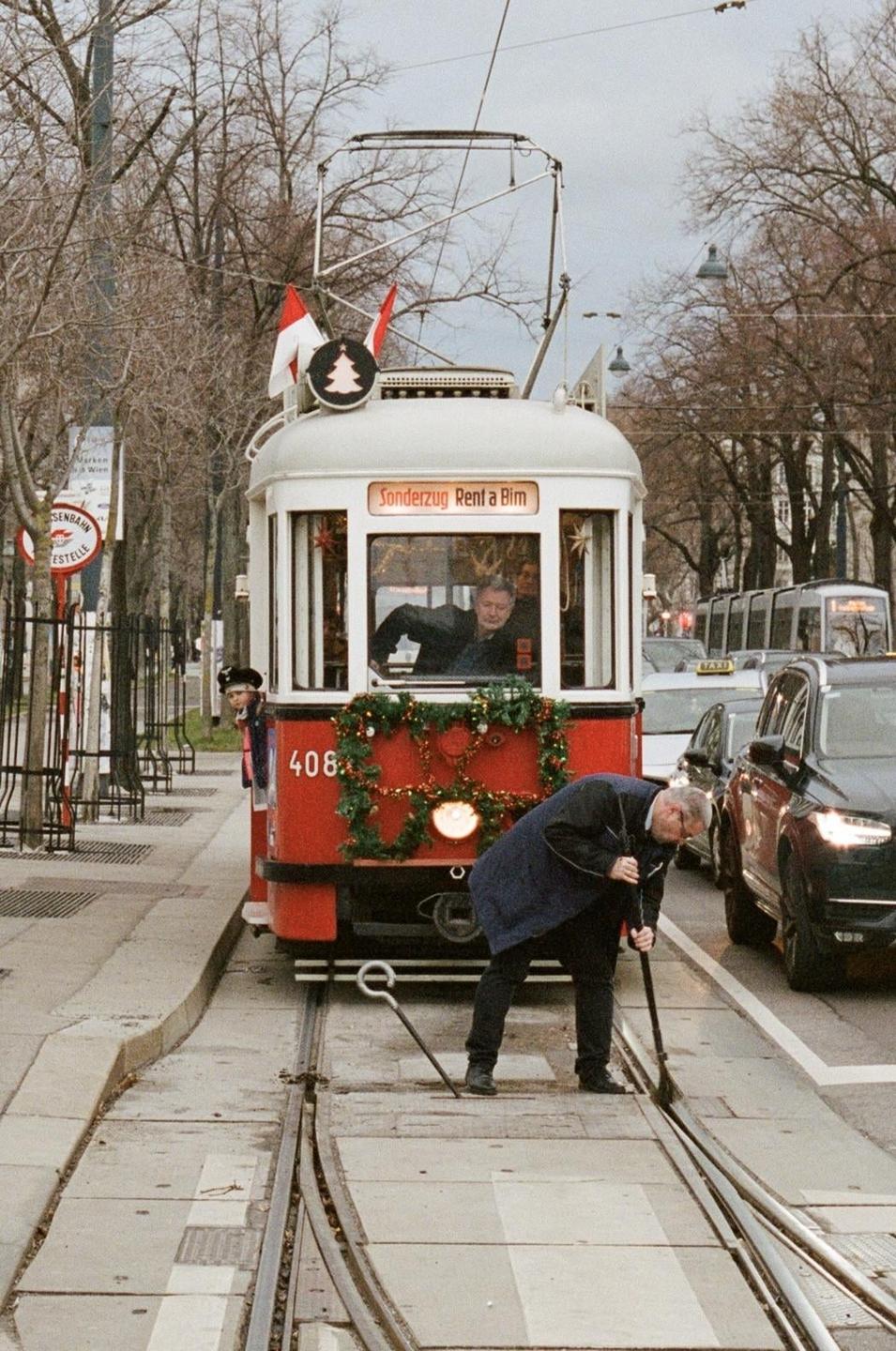 A man bends over to adjust a tram track switch next to a decorated tram.
