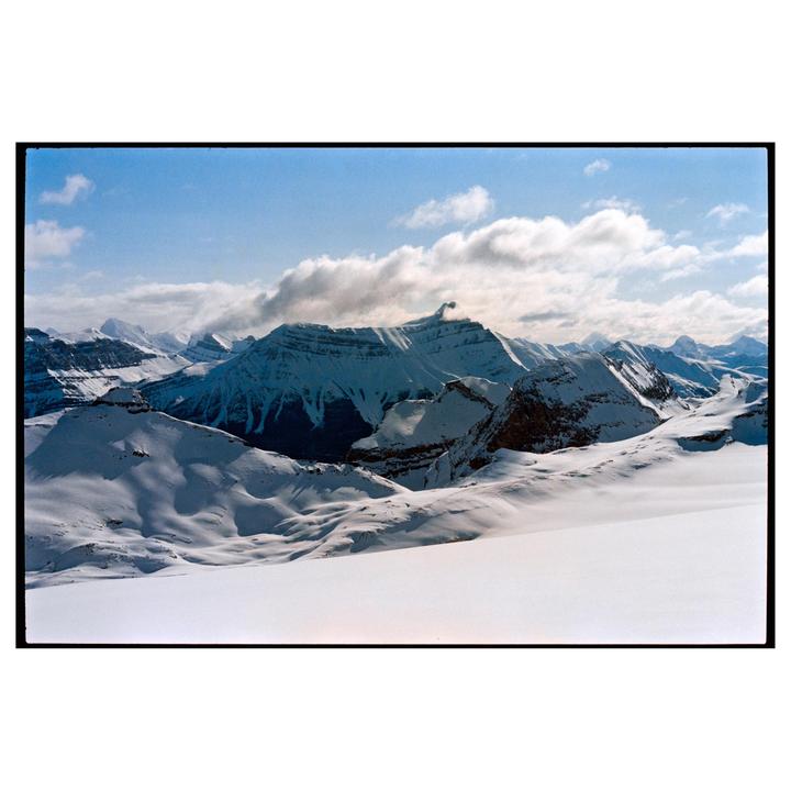 A vast mountain range covered in snow is visible under a partly cloudy sky.