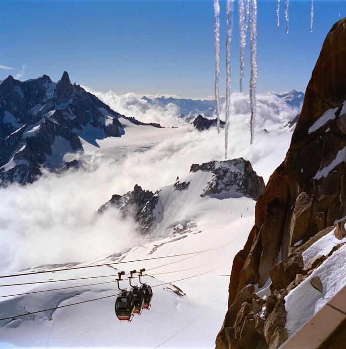 Three cable cars ascend a snowy mountain with clouds and icicles in the foreground.
