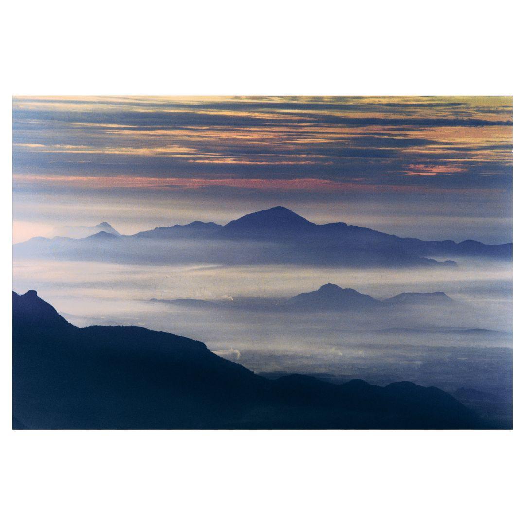 A mountain range is covered in fog under a dramatic sky.