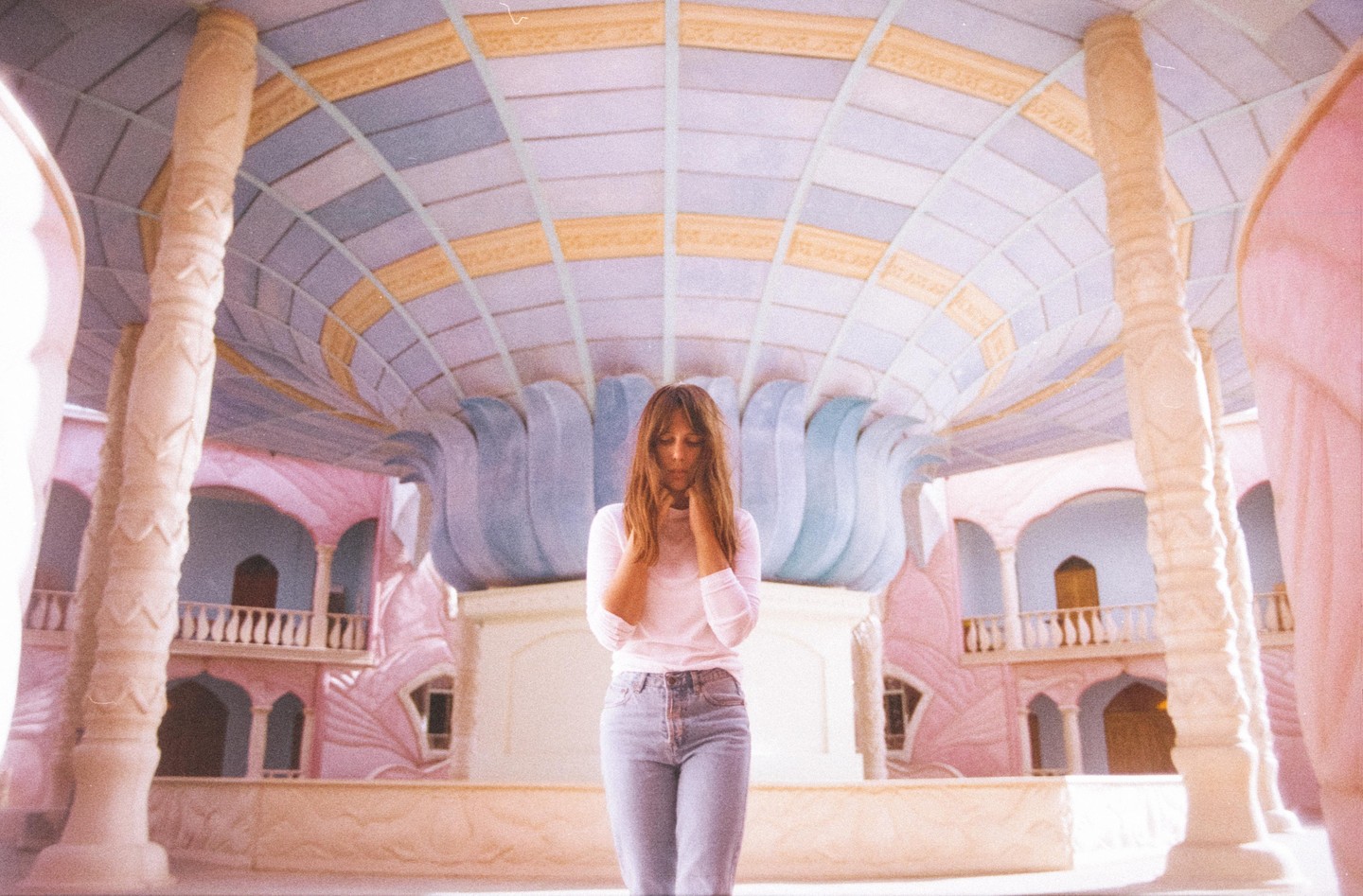 A woman stands in a large, ornate room with a patterned ceiling and decorative pillars.