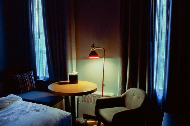 A hotel room is illuminated by a red lamp and blue light from a window.