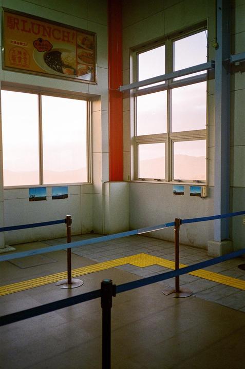 A waiting area with large windows overlooks a hazy mountain landscape, with a "Lunch!" sign and small landscape photos on the wall.
