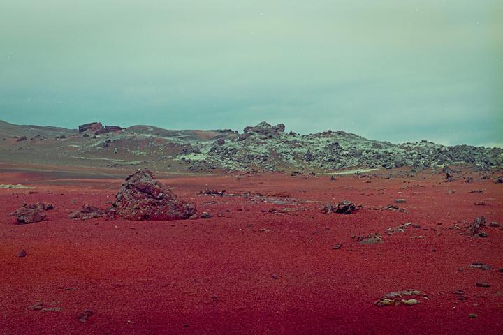 A vast, rocky landscape with red earth stretches under a pale sky.
