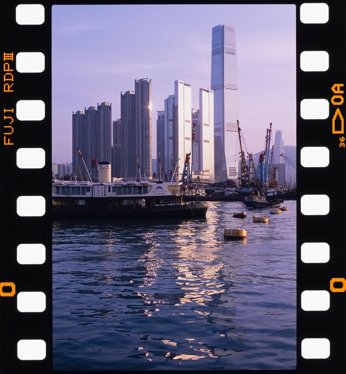 A ferry boat is docked in a harbor with a city skyline in the background.