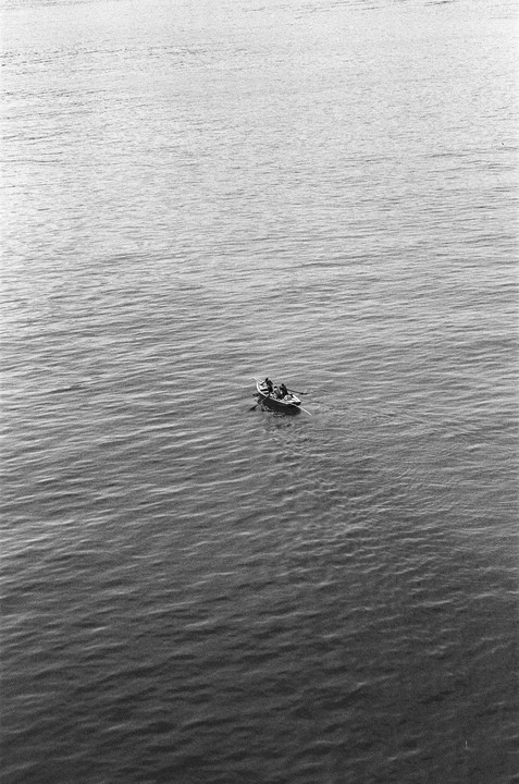 A small boat with two people is in the middle of a vast body of water.
