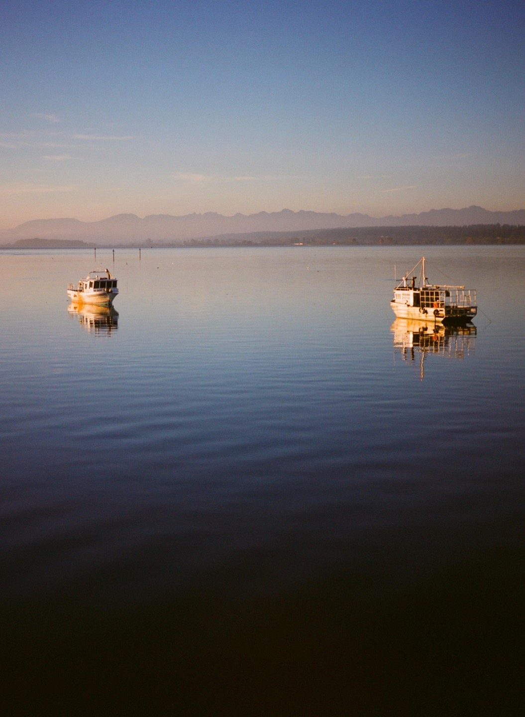 Two boats float on calm water with mountains in the distance under a clear sky.