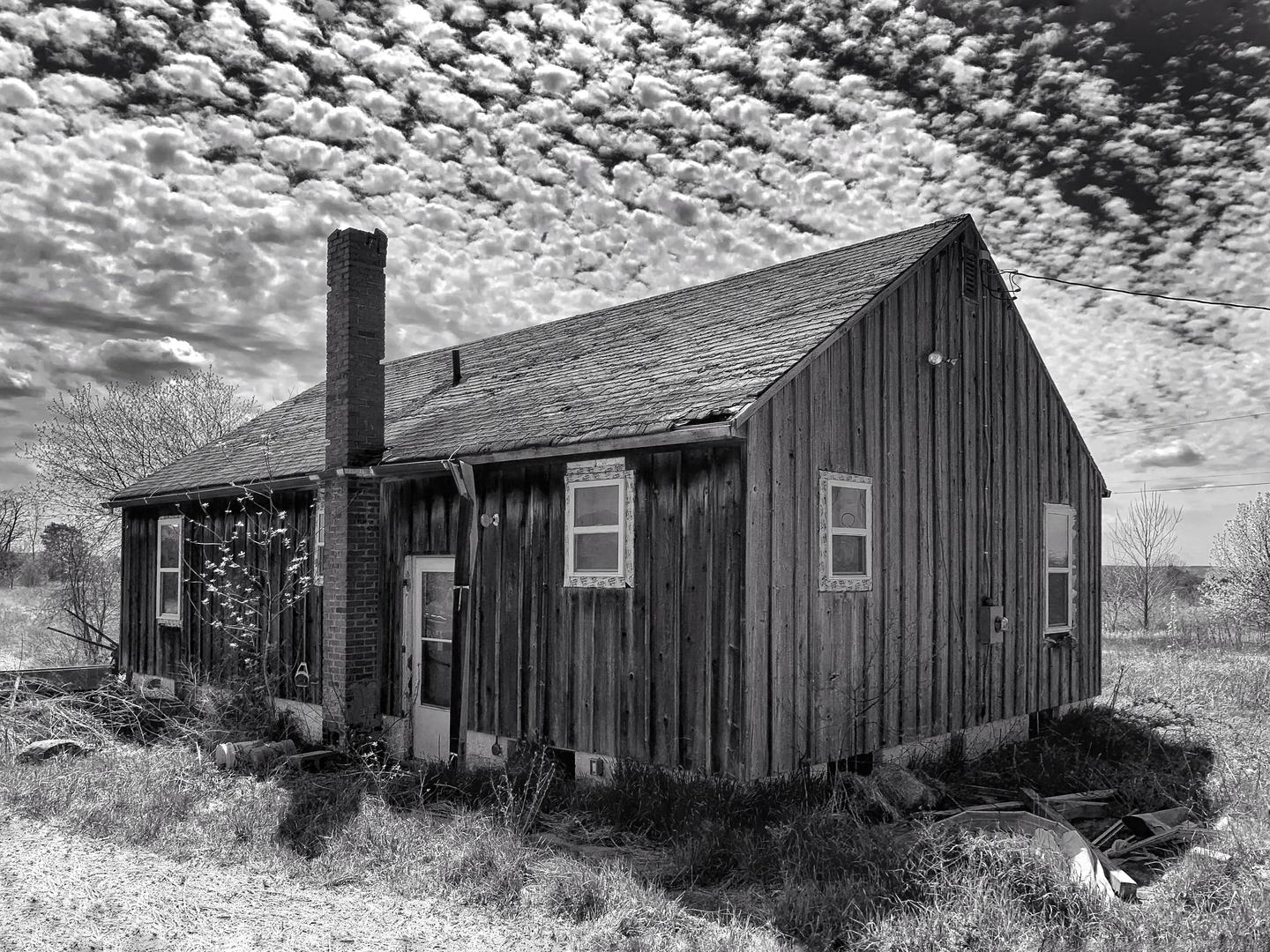An old wooden house with a brick chimney stands under a sky filled with popcorn clouds.