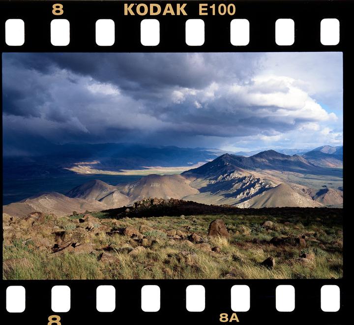 A dramatic landscape shows mountains and valleys under a cloudy sky with patches of sunlight.
