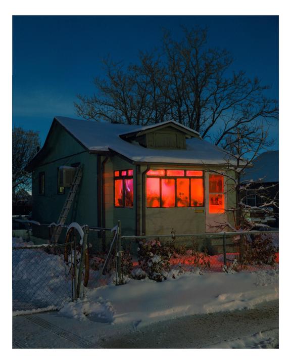 A house with glowing red windows stands in a snowy landscape at night.