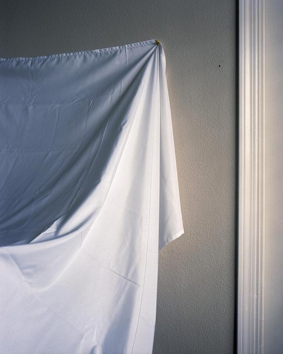 A white sheet hangs against a textured wall next to a white door frame.