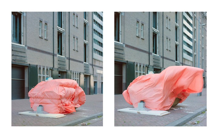 A large pink tarp covers an object on a city street, with a building in the background.