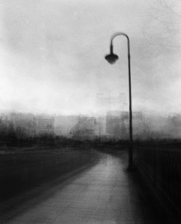 A street lamp stands beside a path with a blurry cityscape in the background.