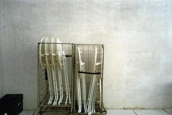 Two metal trolleys filled with white folding chairs stand against a textured white wall.