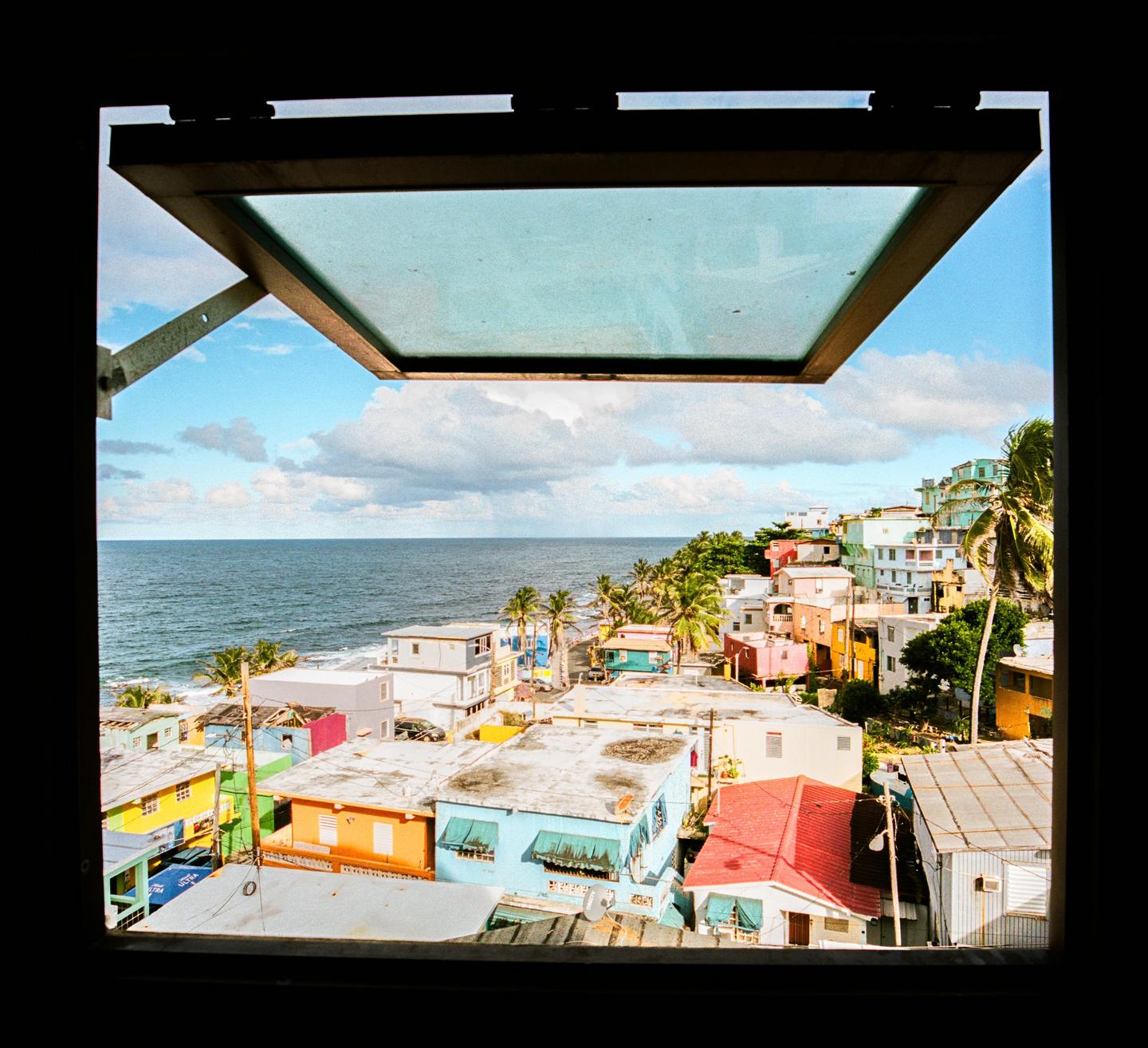 A view of a colorful coastal town and the ocean through an open window.