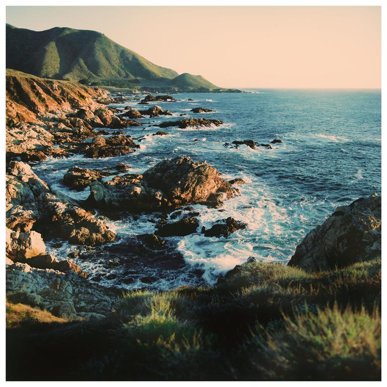 Waves crash against a rocky coastline with mountains in the background.