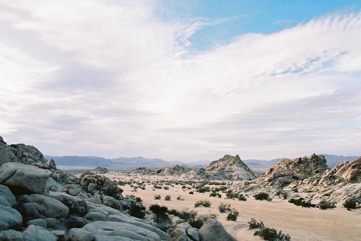 A desert landscape with large rock formations and sparse vegetation stretches under a cloudy sky.