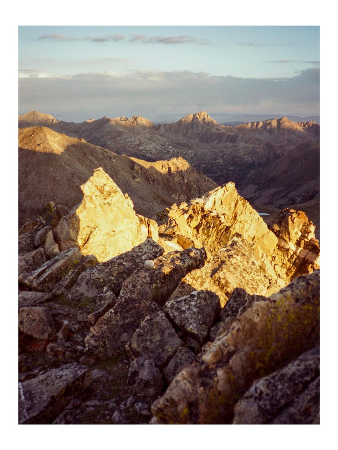A mountain landscape is illuminated by the golden light of the setting sun.