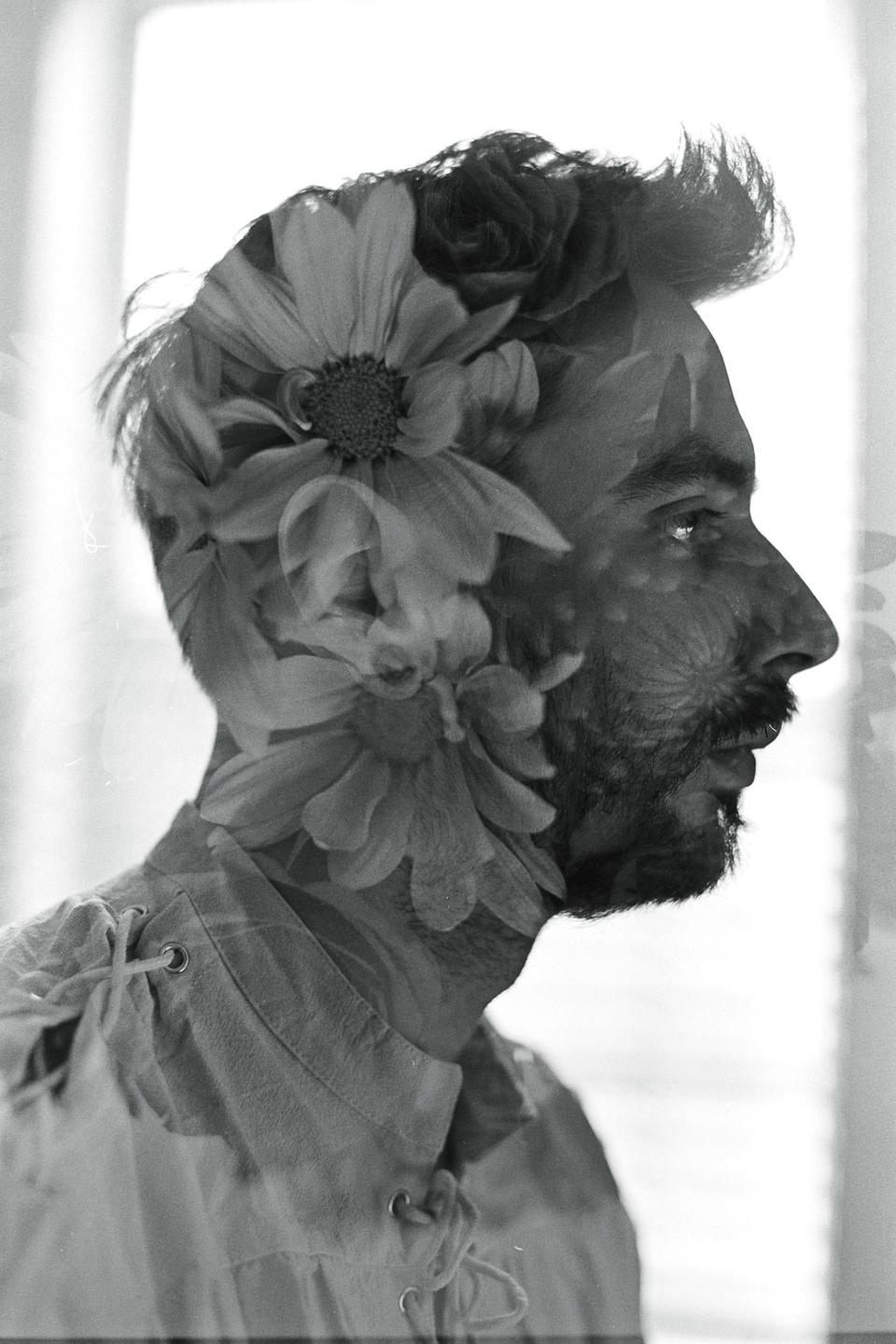 A man's profile is superimposed with flowers in a black and white double exposure.