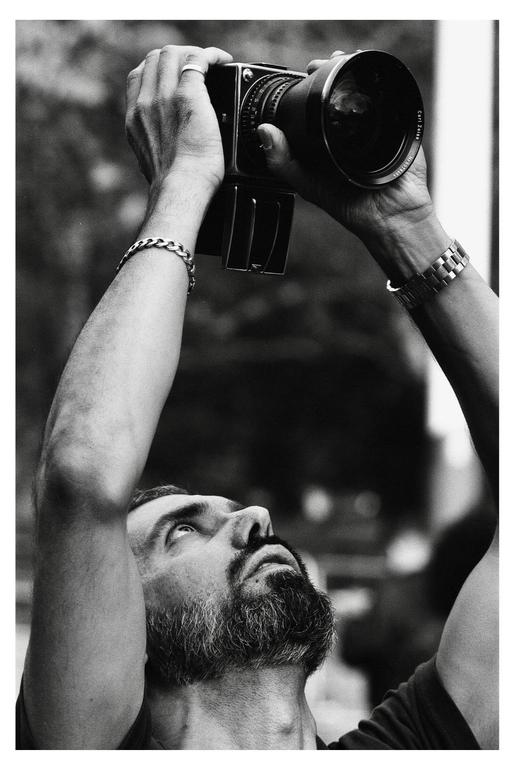 A man with a beard holds a camera above his head, looking up at it.