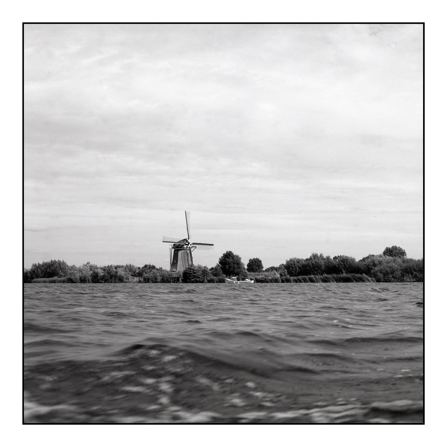 A windmill stands on the far bank of a body of water, with a small boat docked nearby.
