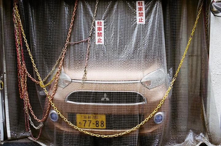 A car is parked behind a clear plastic curtain with chains draped over it.