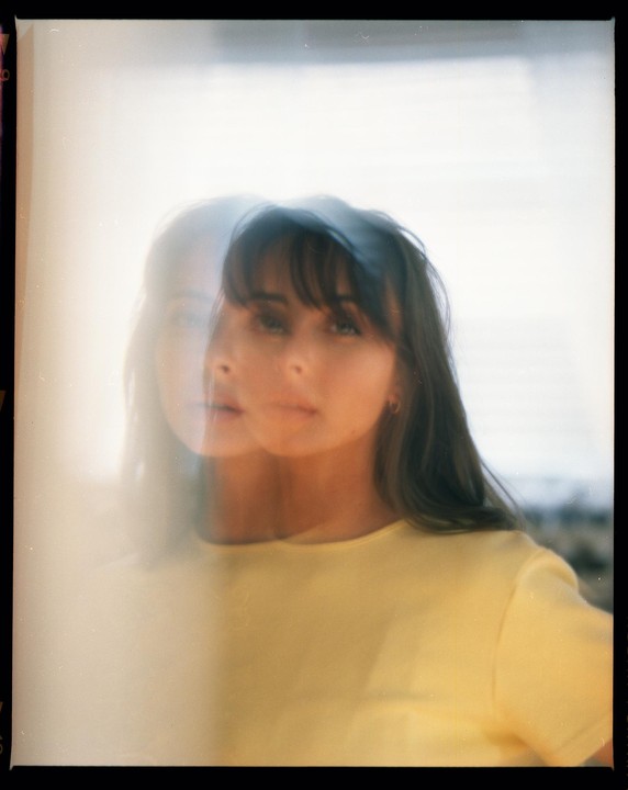 A woman with bangs and long hair is visible through a double exposure.