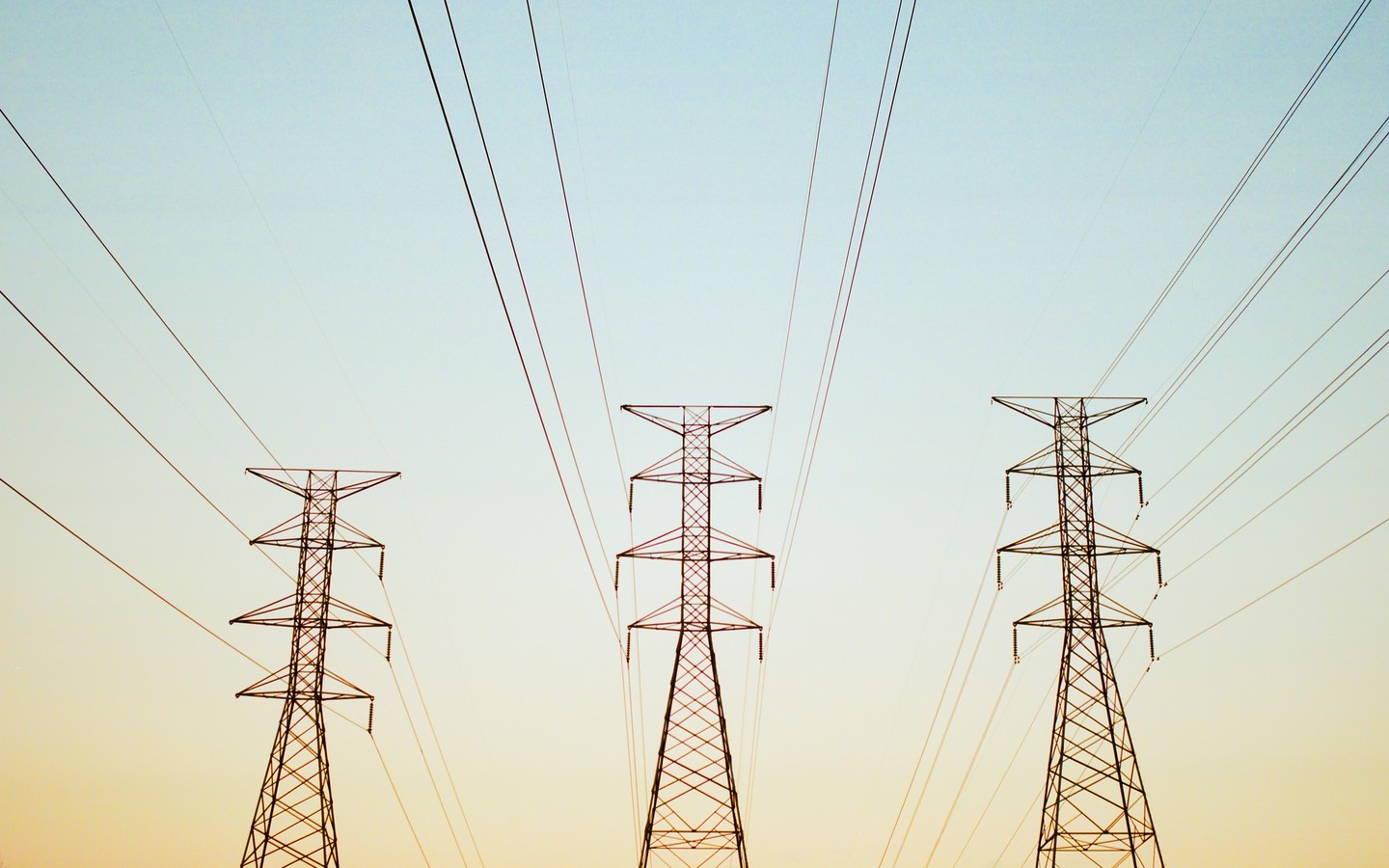 Three electricity pylons stand against a clear sky with power lines extending from them.