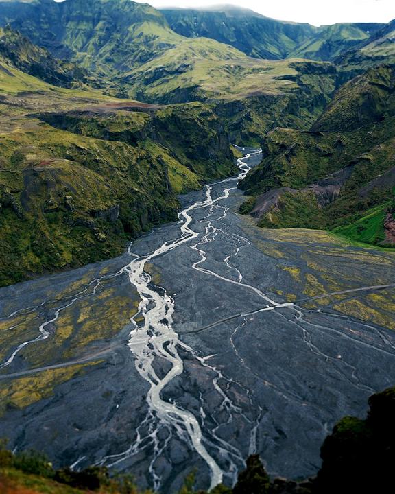 A winding river flows through a valley surrounded by green mountains.